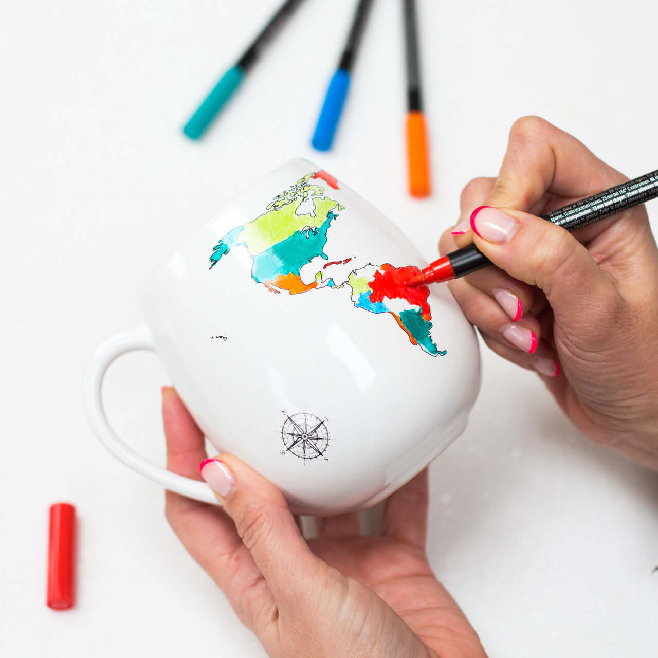 Person coloring a world map on a mug with markers.