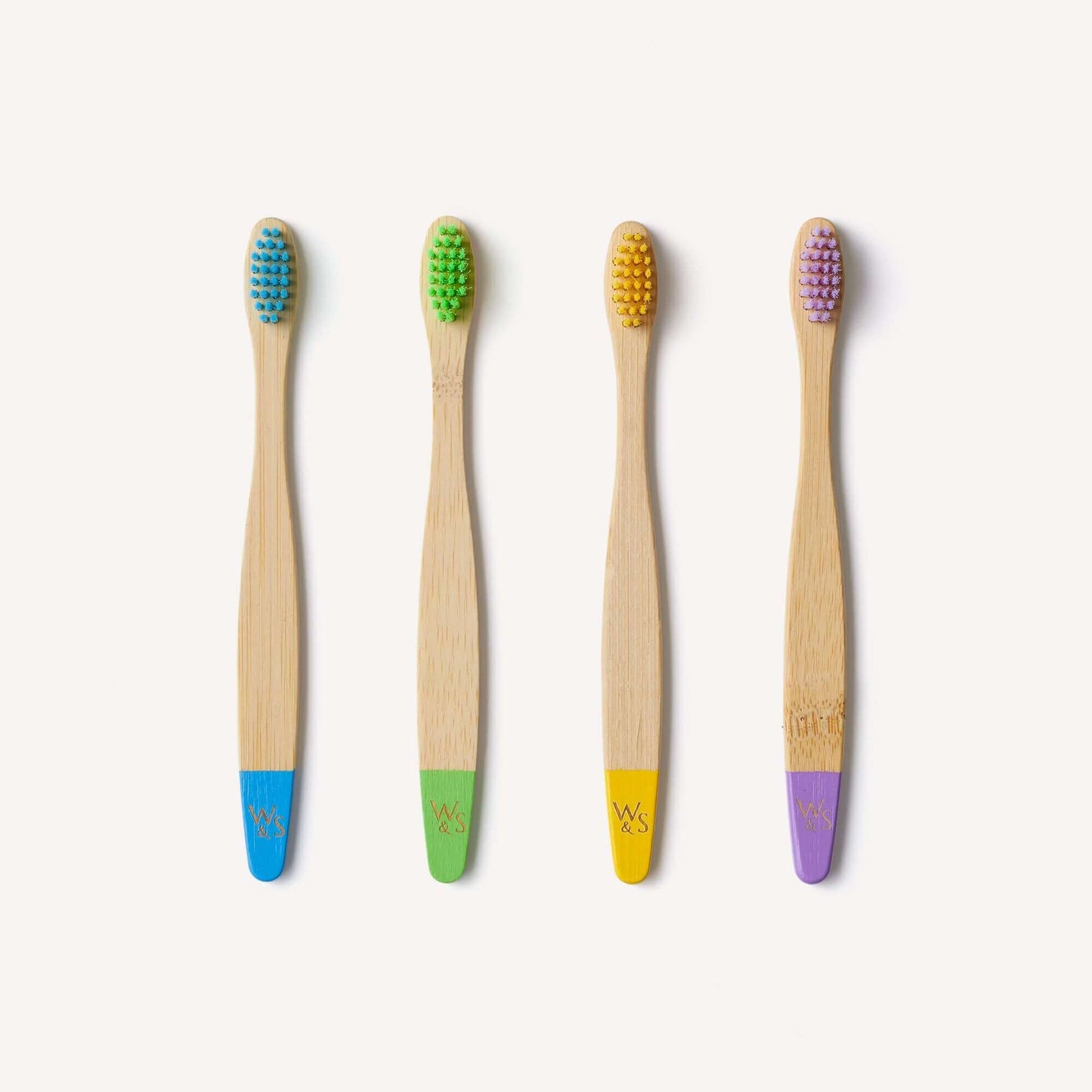 Four bamboo toothbrushes with colored bristle heads on a white background