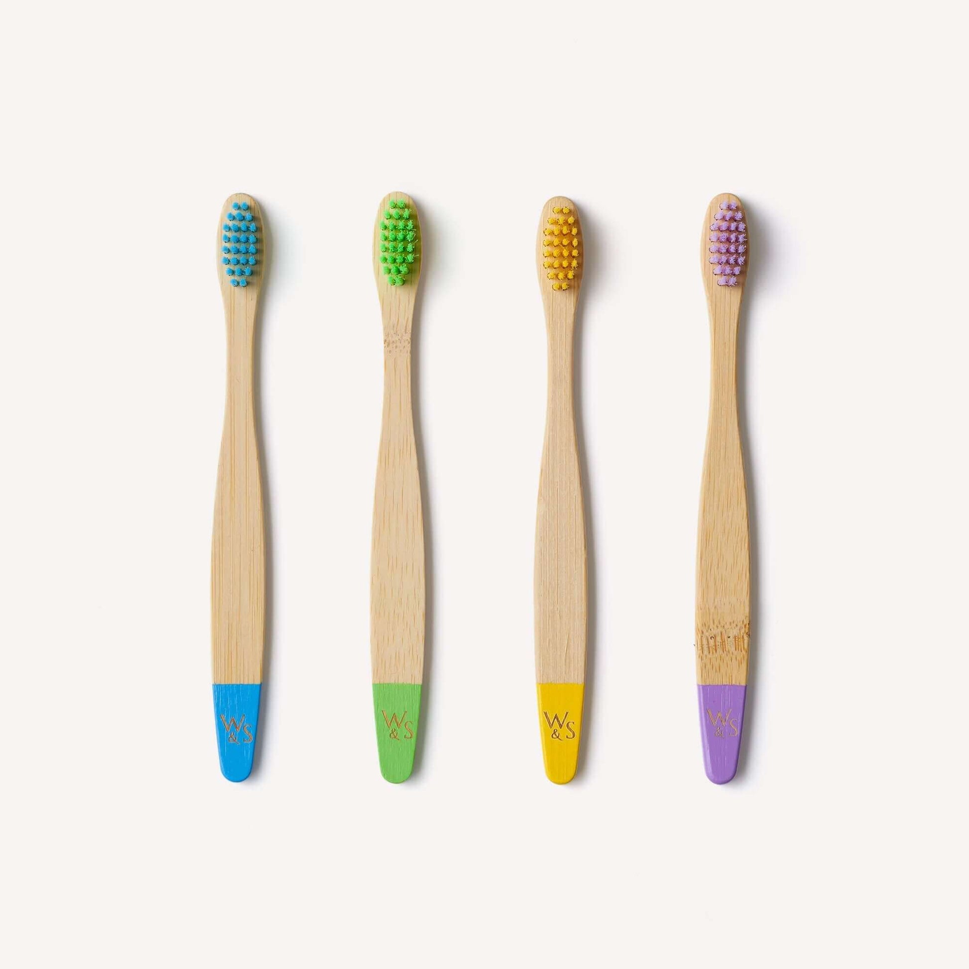 Four bamboo toothbrushes with colored bristle heads on a white background