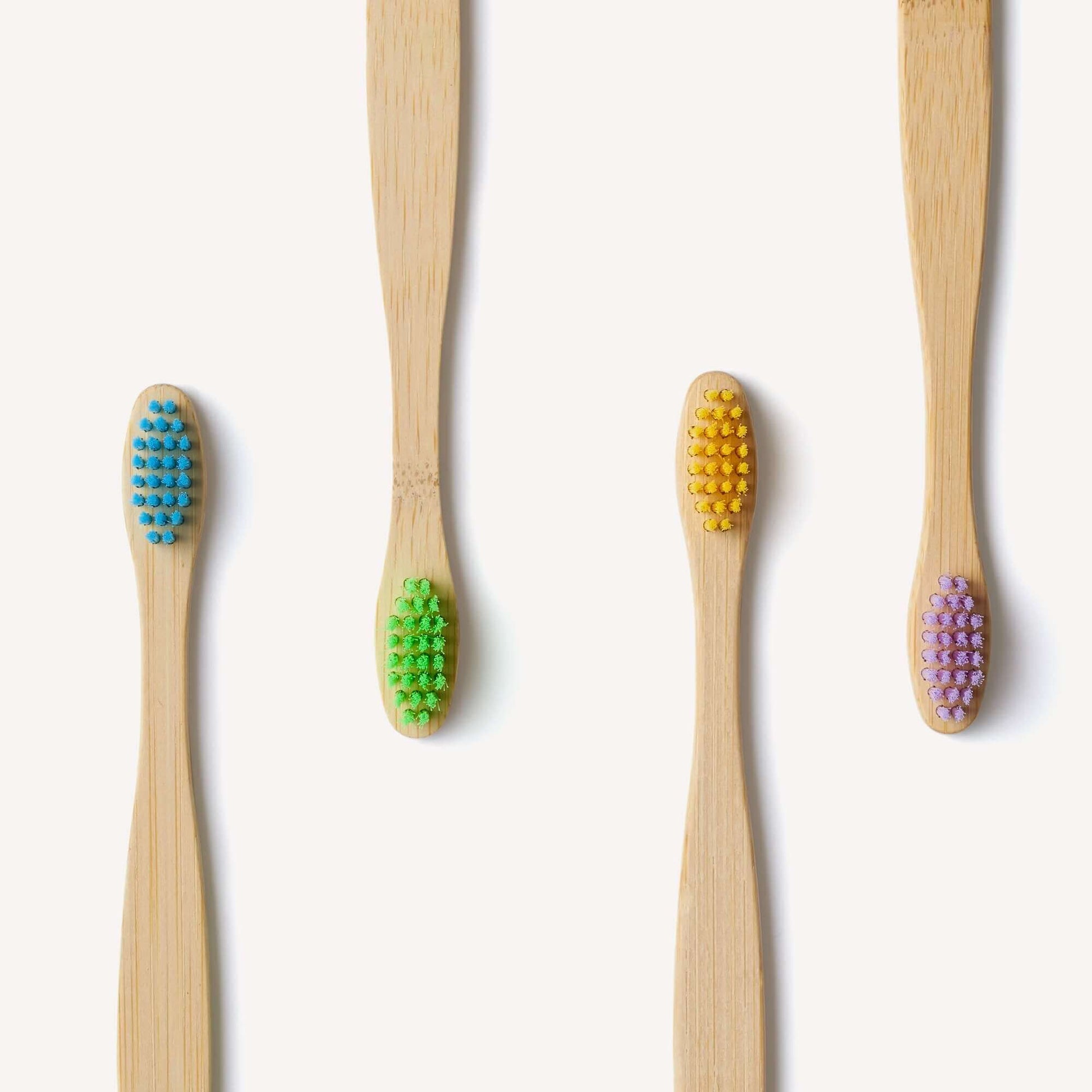 Set of four bamboo toothbrushes with colored bristles on a white background
