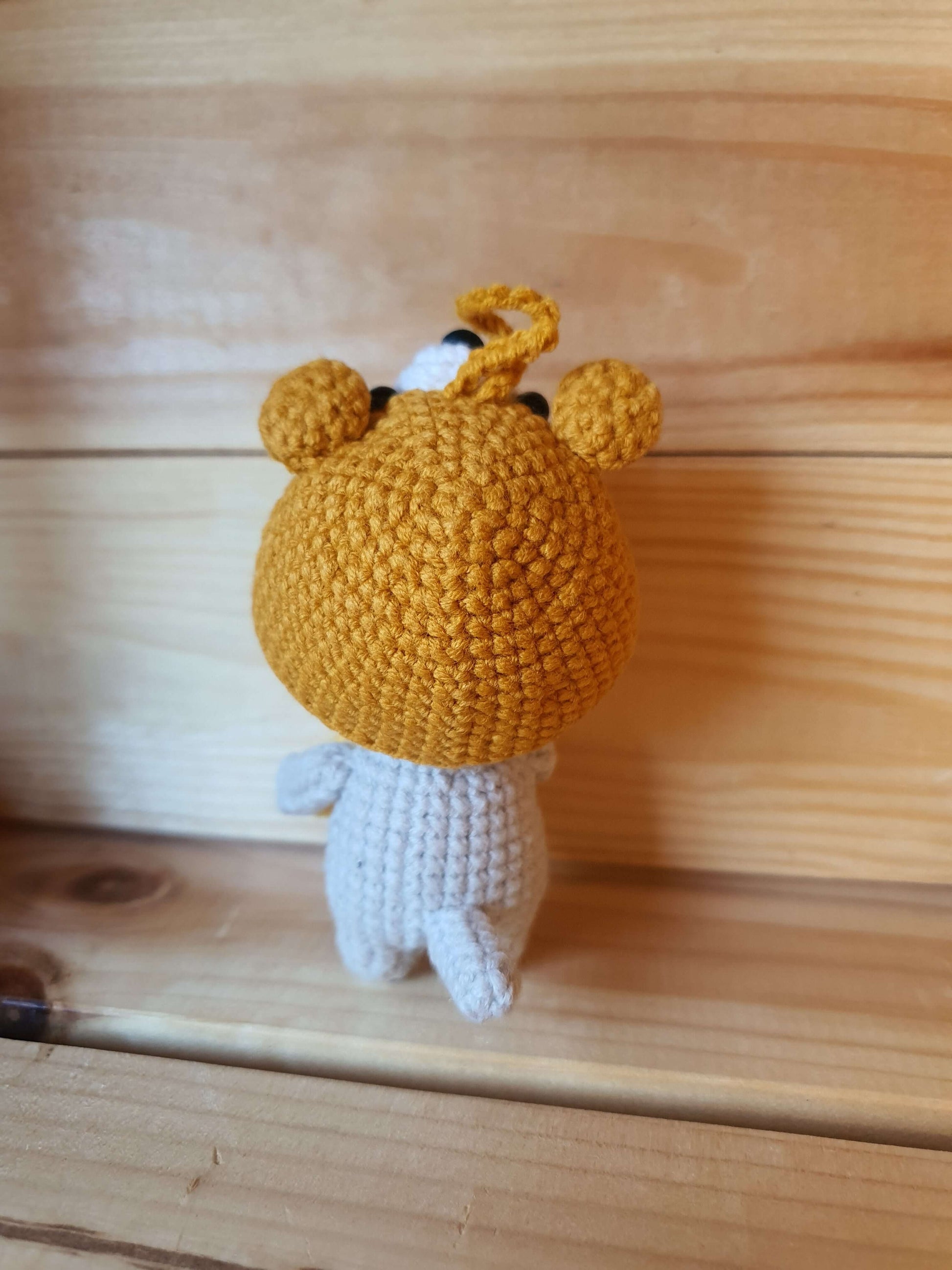 Crocheted toy with a mustard yellow hat on a wooden surface