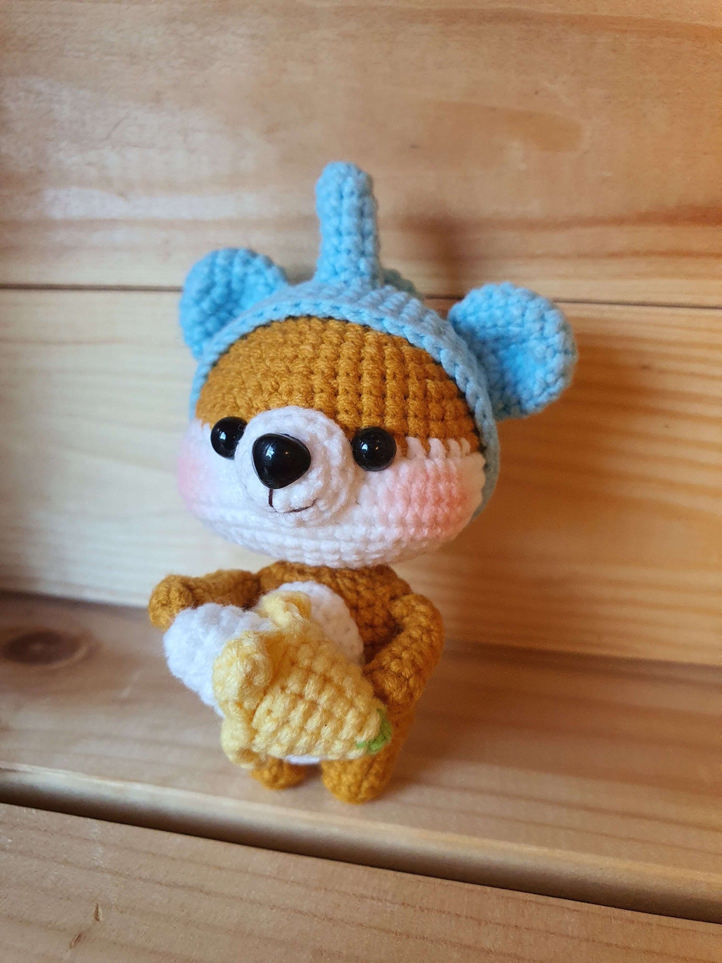Small crochet bear toy with a blue hat on a wooden surface