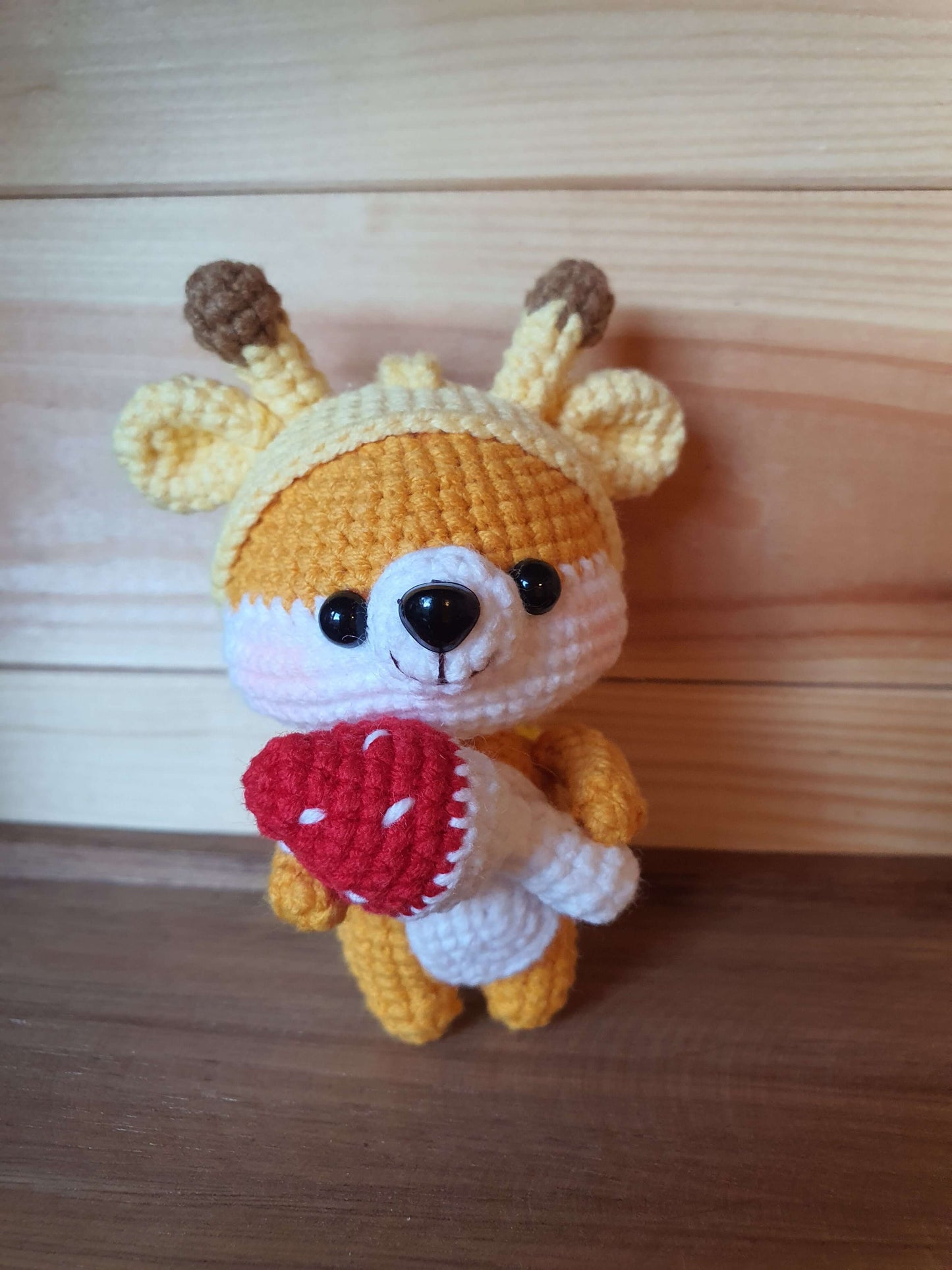 Crocheted deer toy with a red heart on a wooden surface