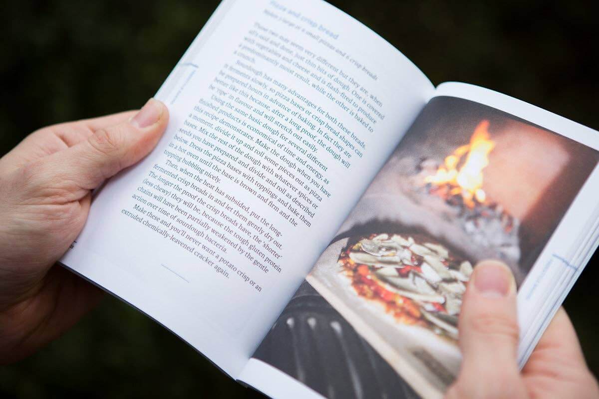 Open book with text and a photograph of food over a fire held by a person.