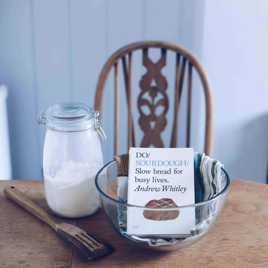 Bowl with a label, jar of flour, and wooden spoon on a table.