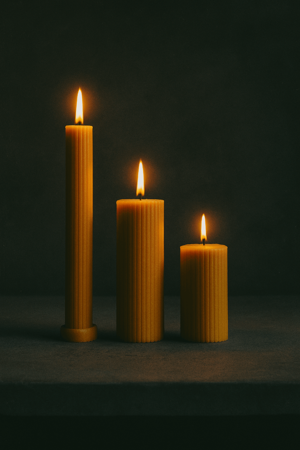 Cylinders: set of 3 beeswax pillar candles in different heights, glowing with warm candlelight on a dark background.