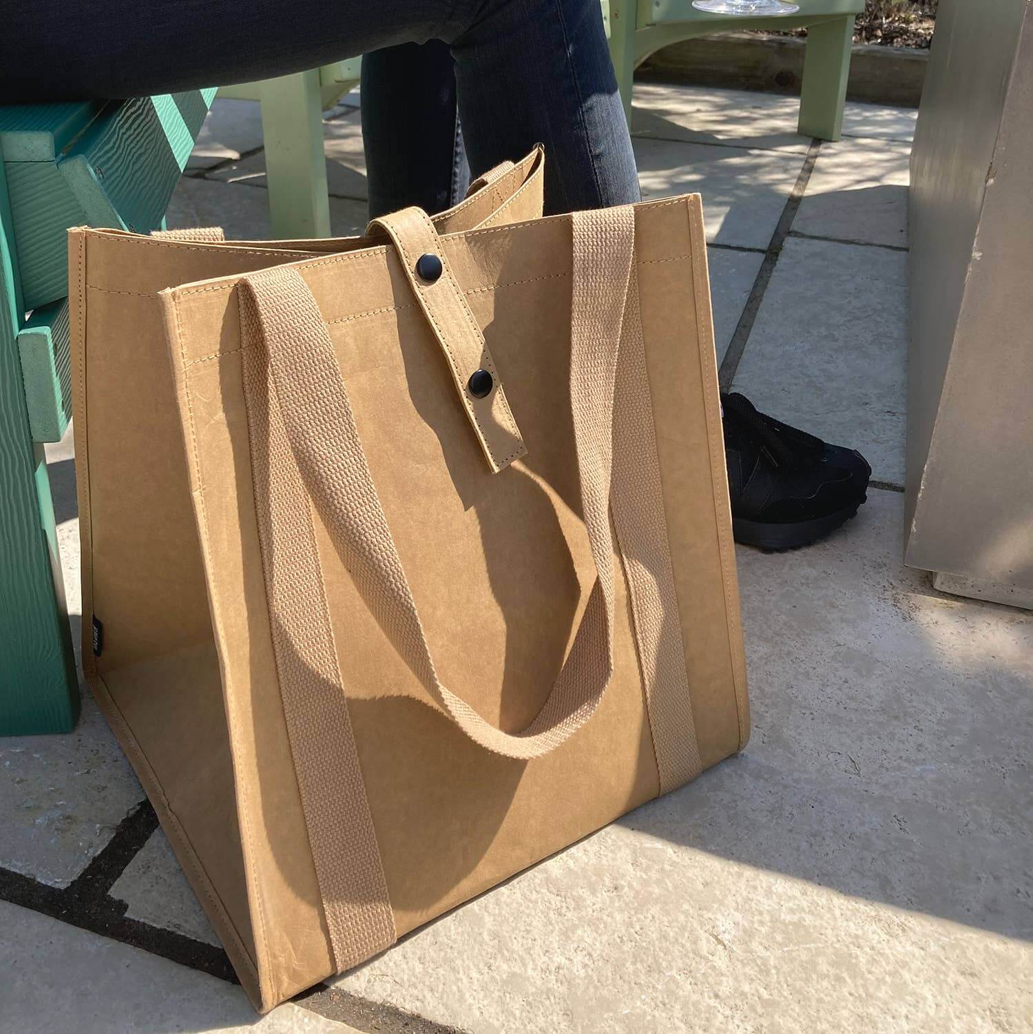 Brown tote bag on a concrete surface with a person partially visible in the background.