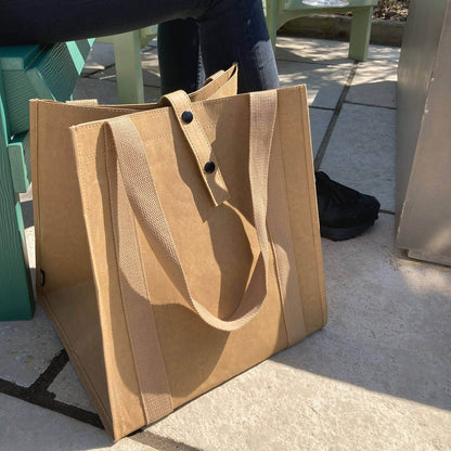 Brown tote bag on a concrete surface with a person partially visible in the background.