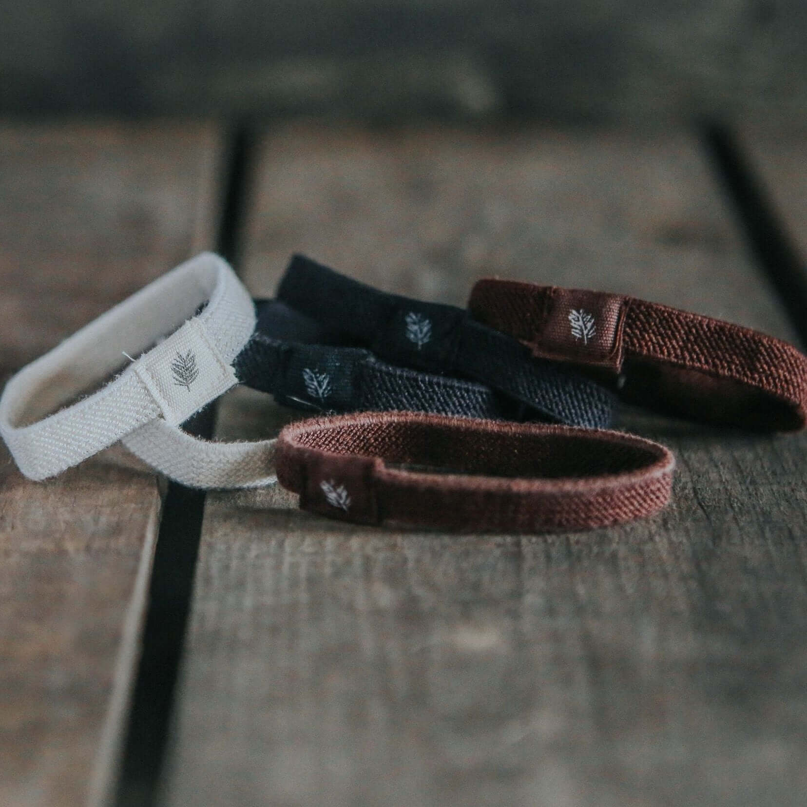 Three woven bracelets in white, black, and brown on a wooden surface.