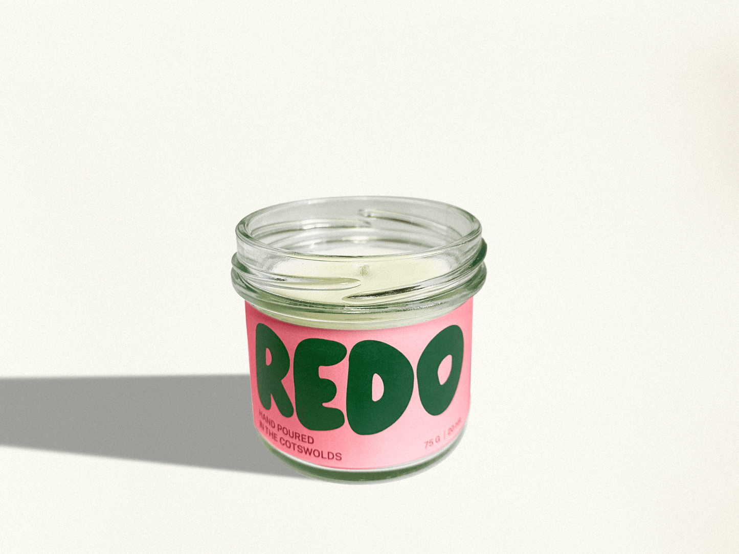 Candle in a glass jar with a pink label and green text on a white background