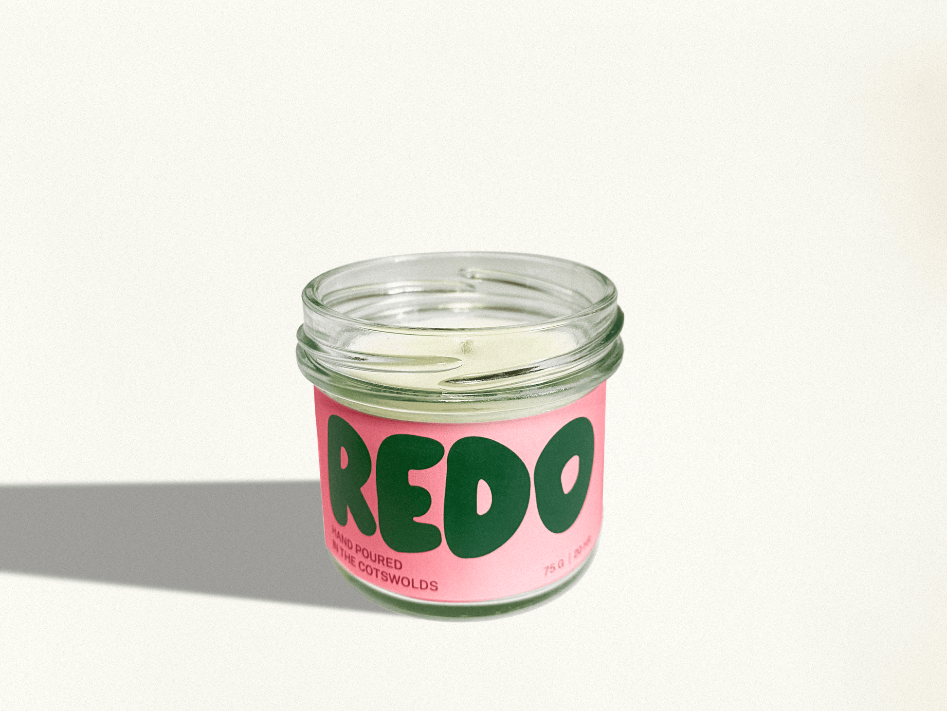 Candle in a glass jar with a pink label and green text on a white background