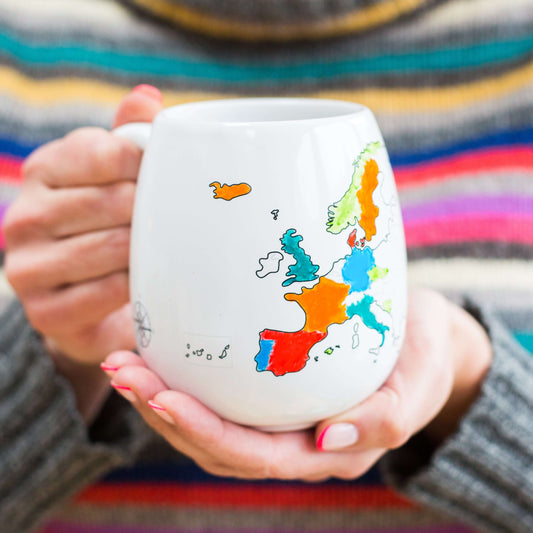 Person holding a mug with a colorful map design against a striped background