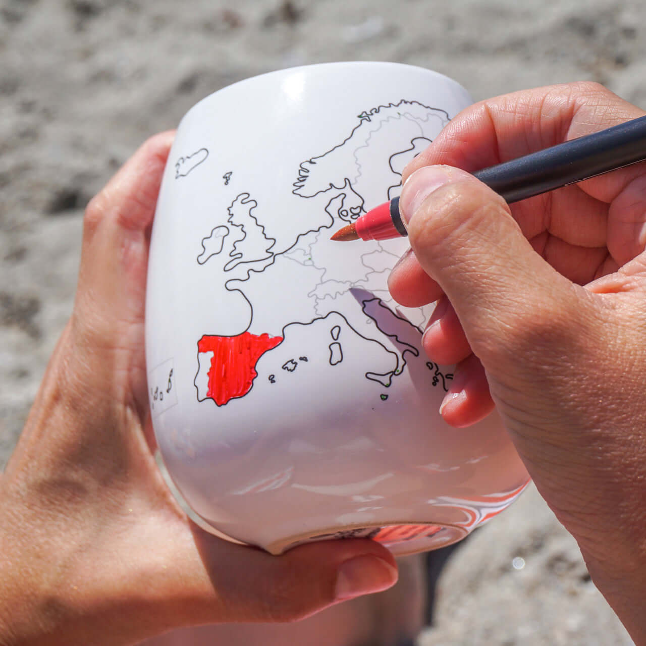 Person coloring a map of Europe on a white mug with a red pen.