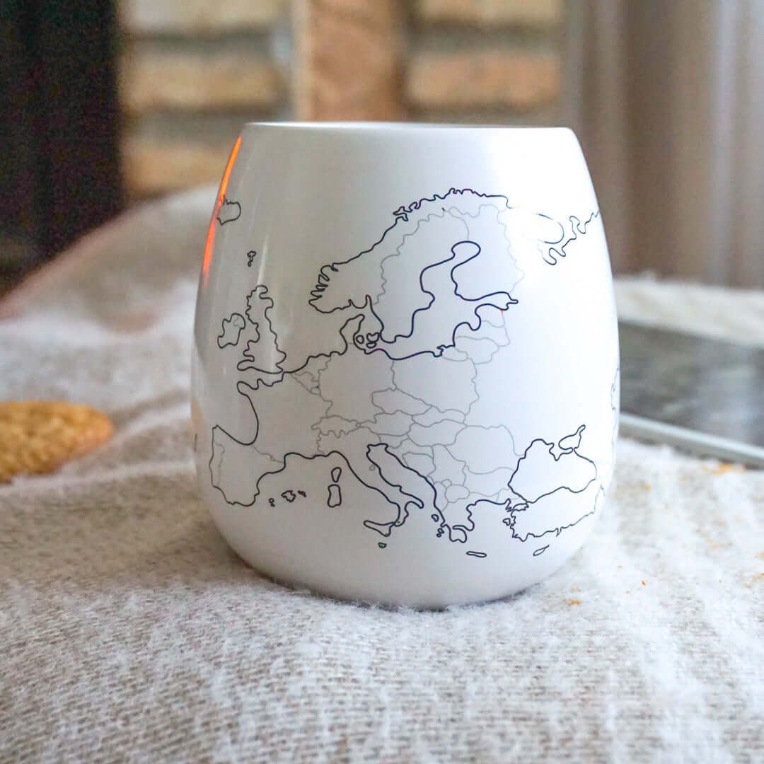 White mug with a black outline map of Europe on a textured surface.