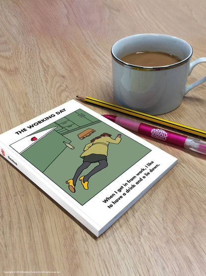Modern Toss Work Lie Down A6 notebook on a wooden desk beside a mug and pencils