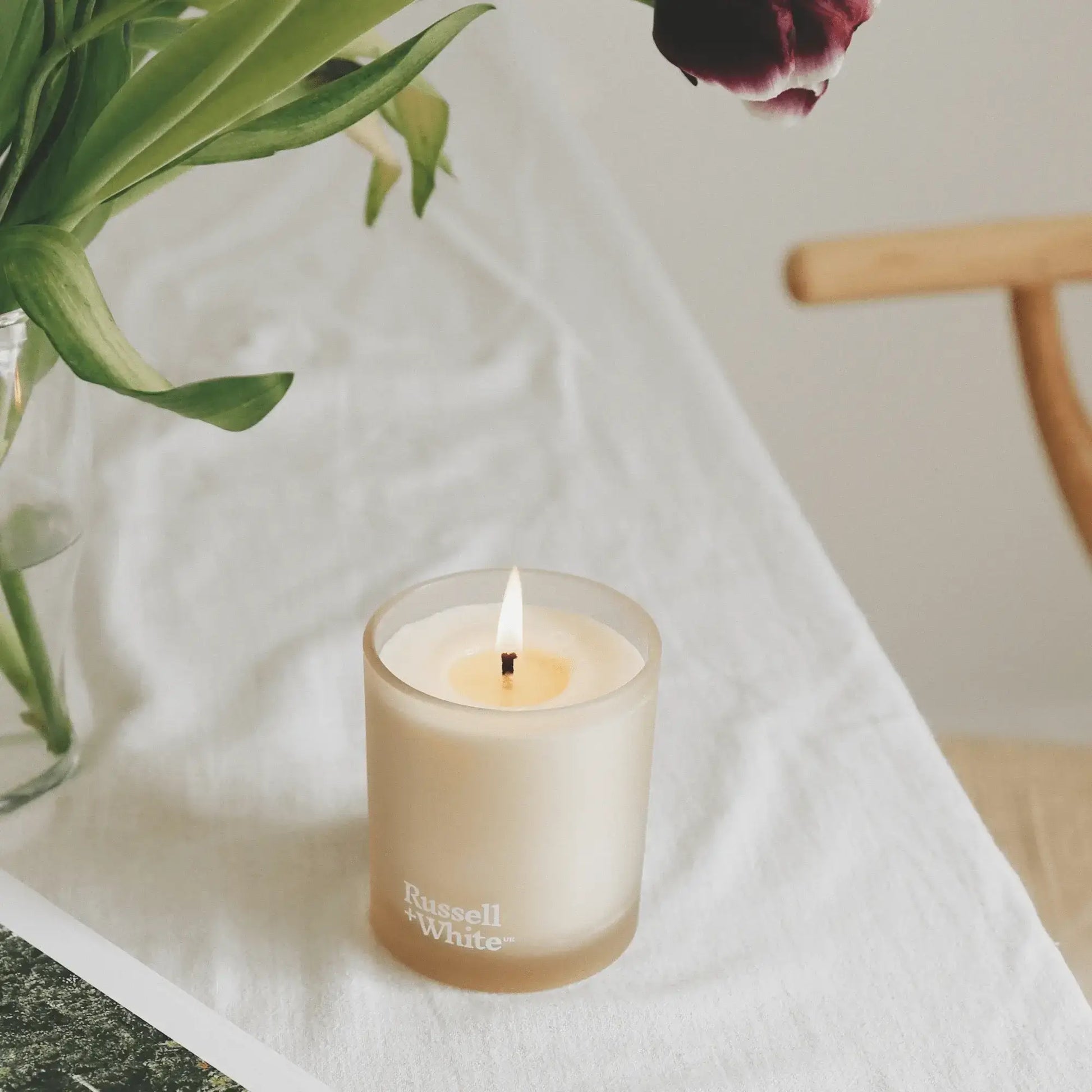 Soy wax candle with a lit flame on a table, surrounded by flowers, emphasizing the Florale scent.