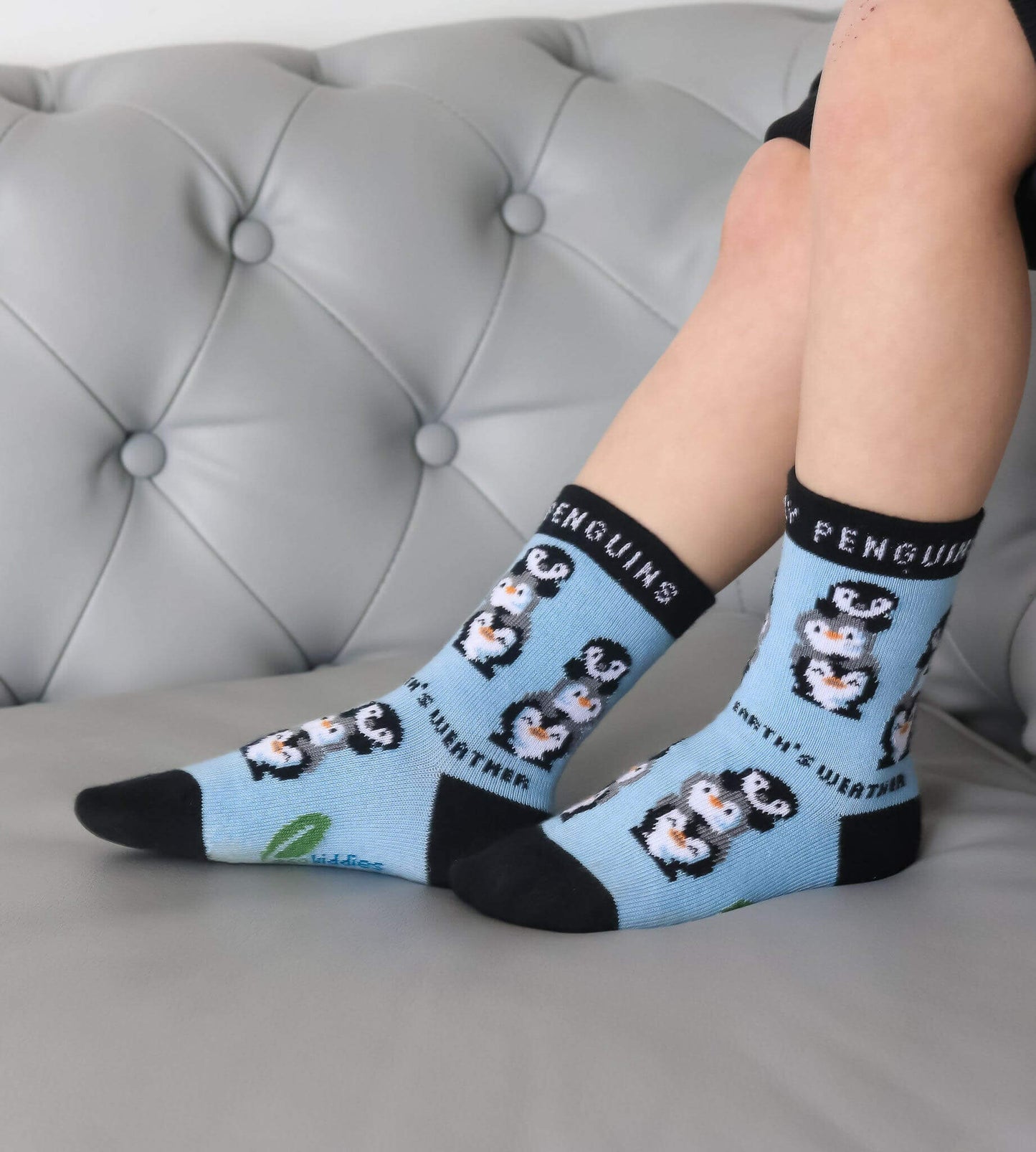 Person wearing light blue socks with penguin design on a gray couch.