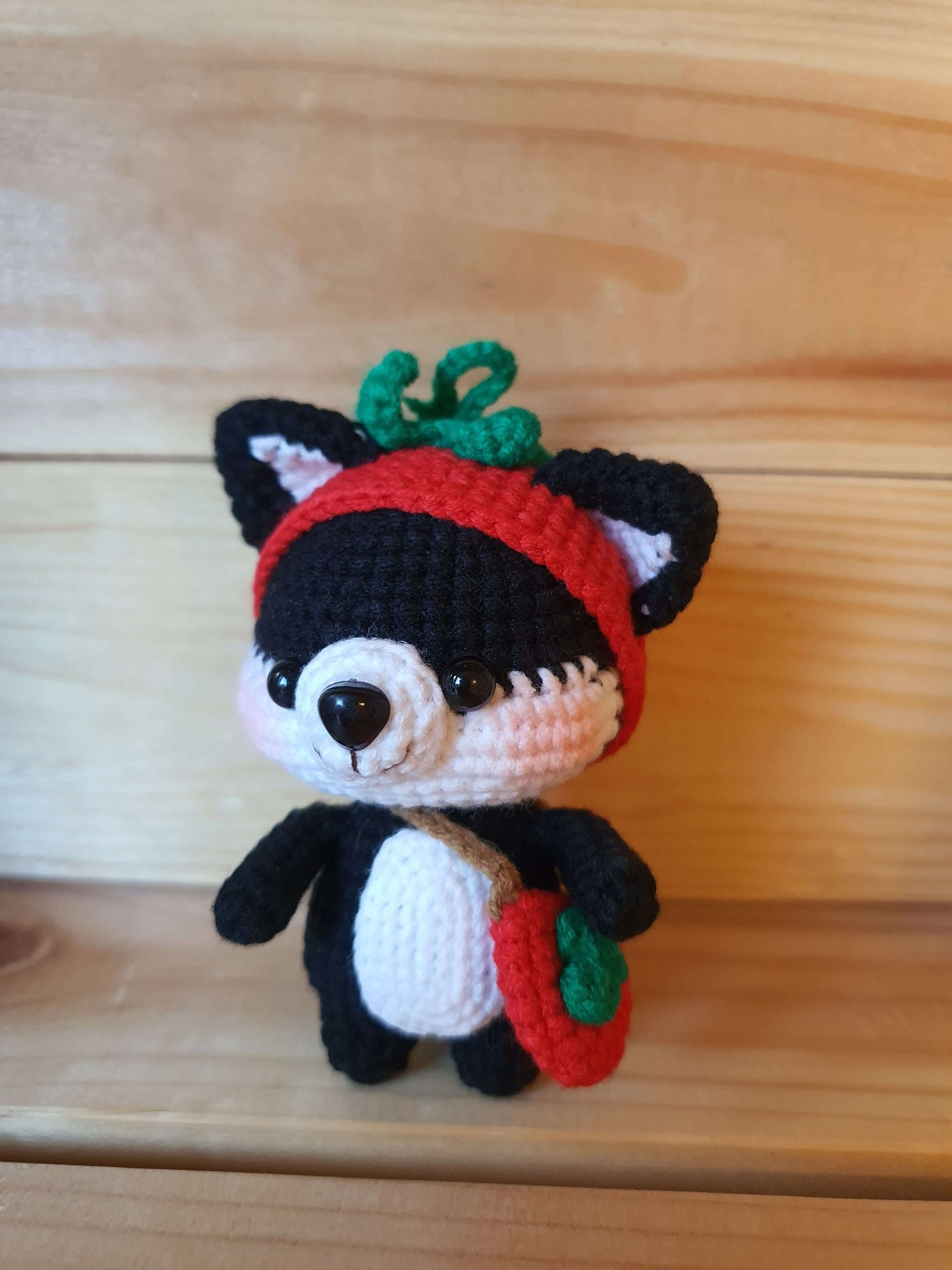Crocheted fox toy with a red hat on a wooden surface