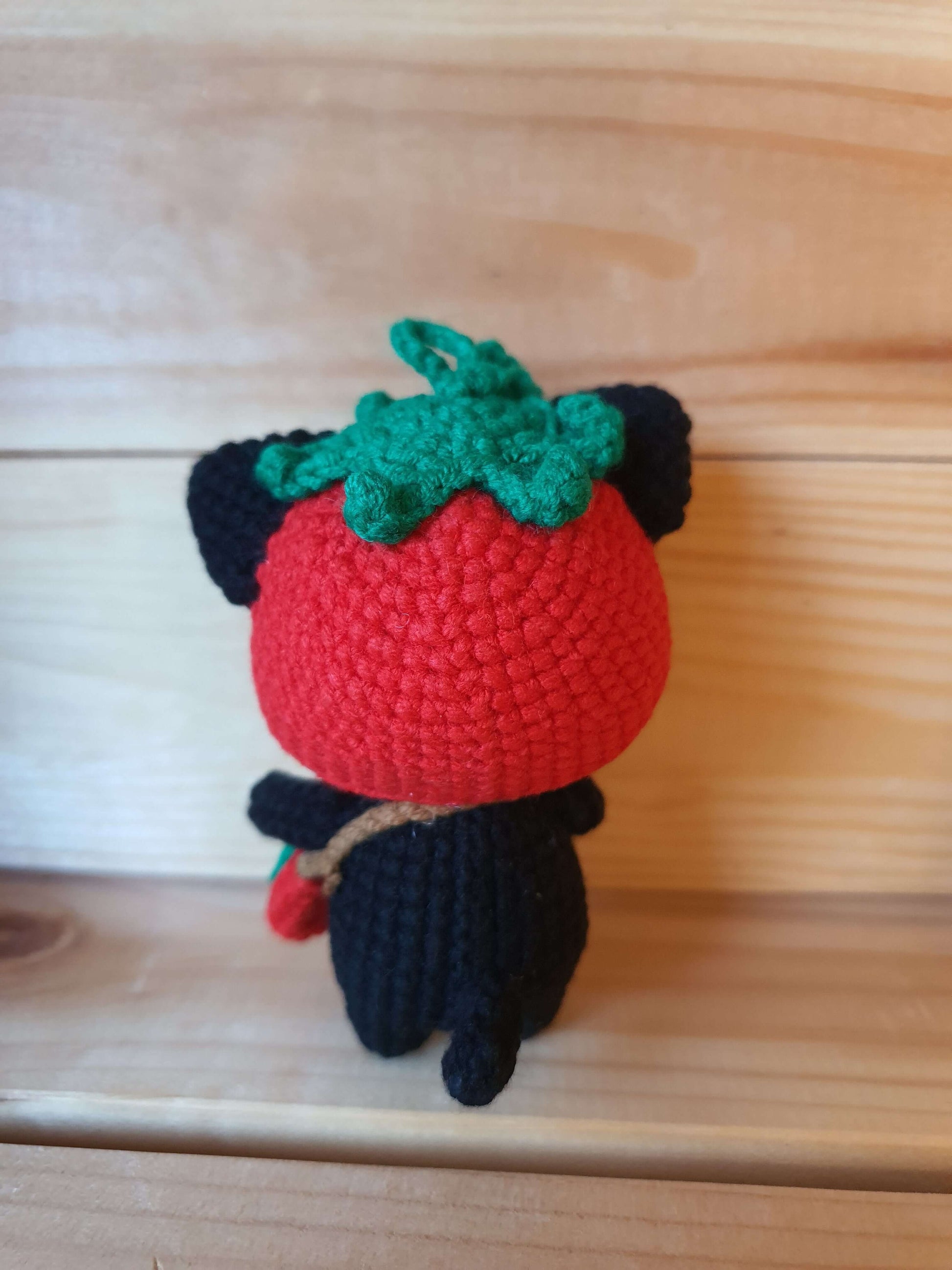 Crocheted strawberry-shaped character on a wooden surface