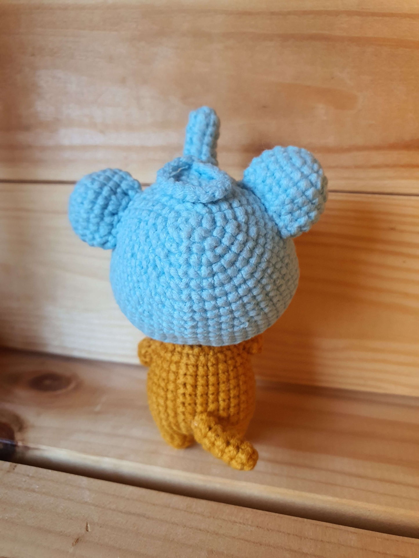 Crocheted blue and yellow character on a wooden surface