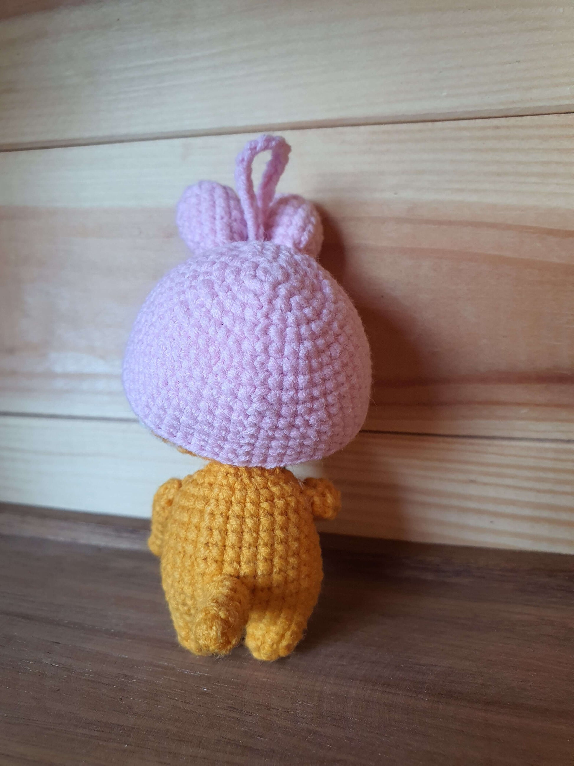 Crocheted character with a pink top and yellow bottom on a wooden surface