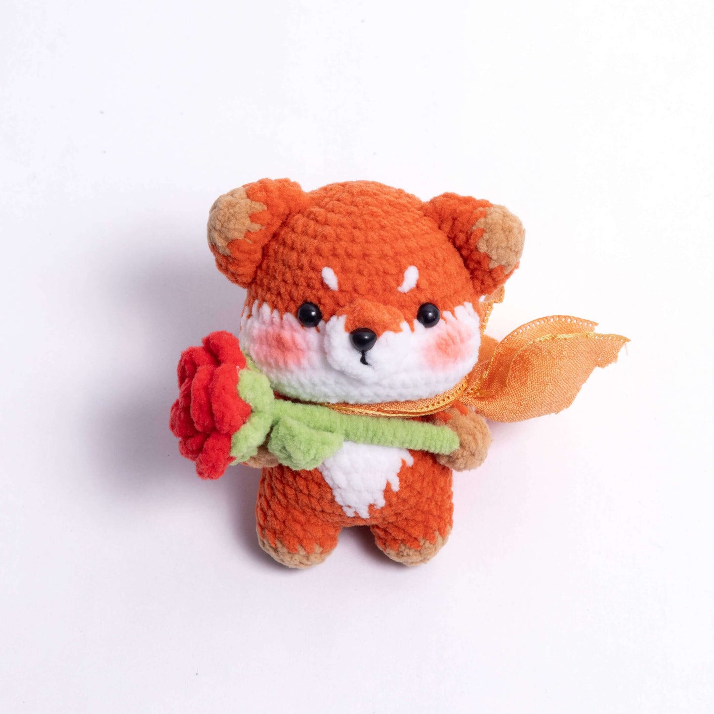 Crocheted fox toy holding a red rose on a white background