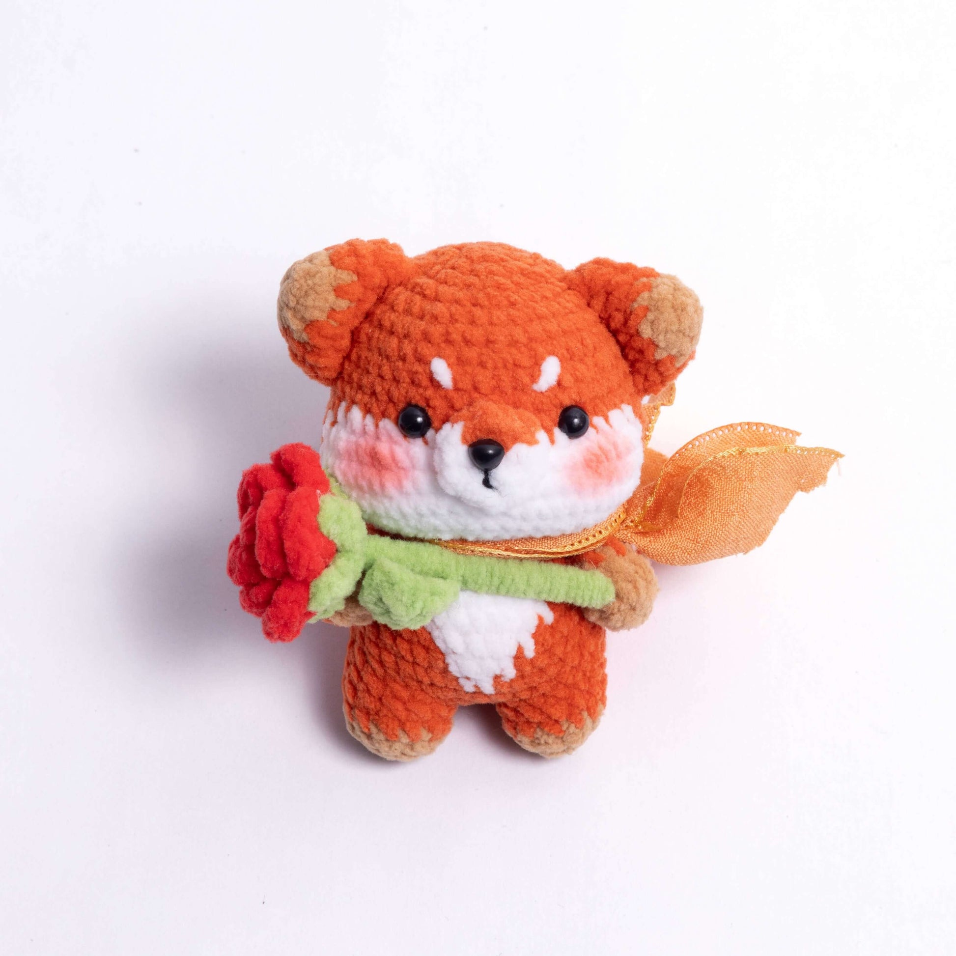 Crocheted fox toy holding a red rose on a white background