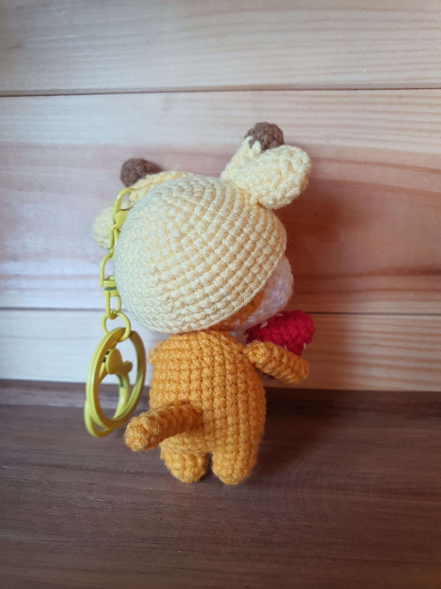 Crocheted bear keychain with a white hat on a wooden surface