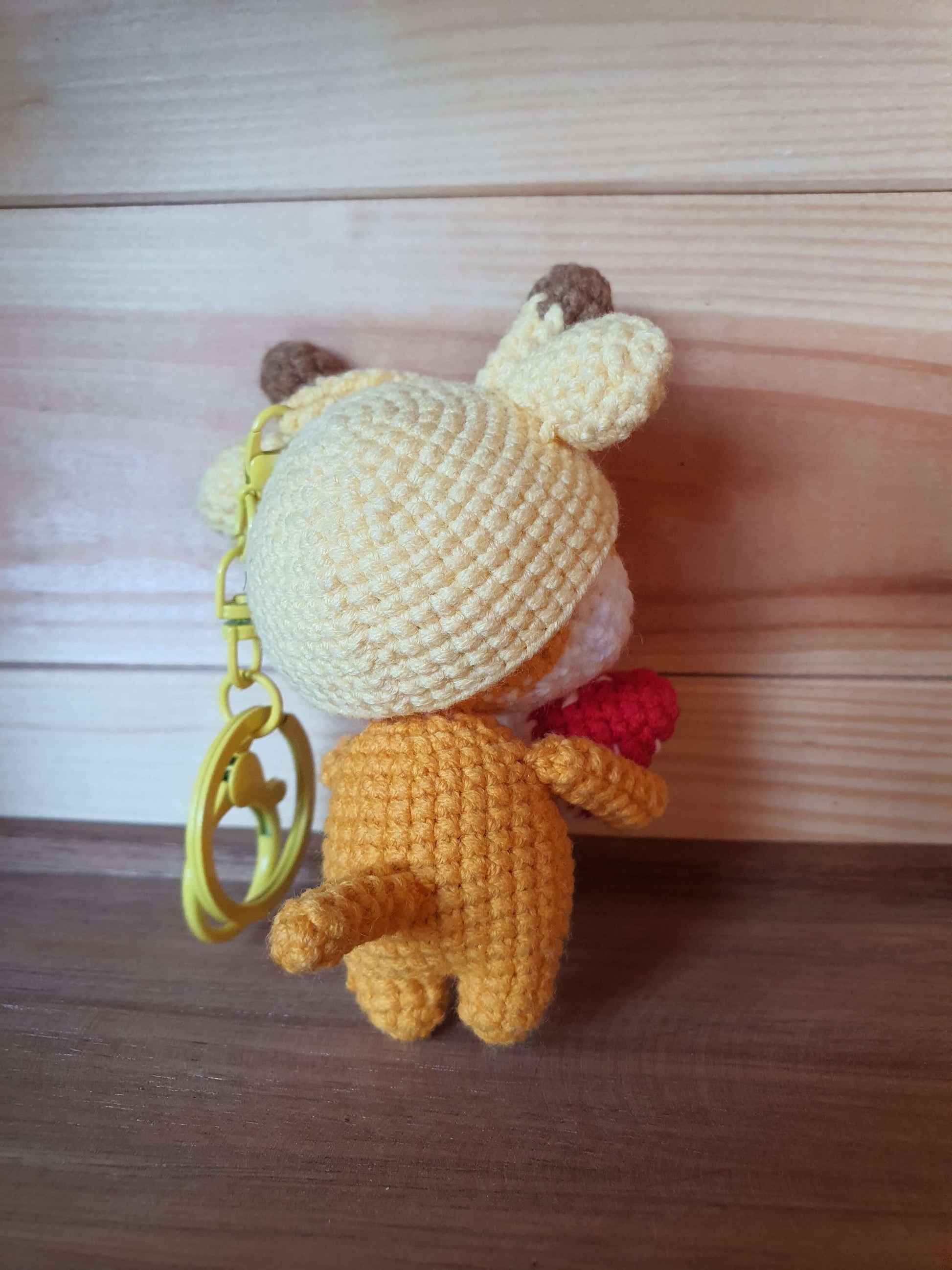 Crocheted bear keychain with a white hat on a wooden surface
