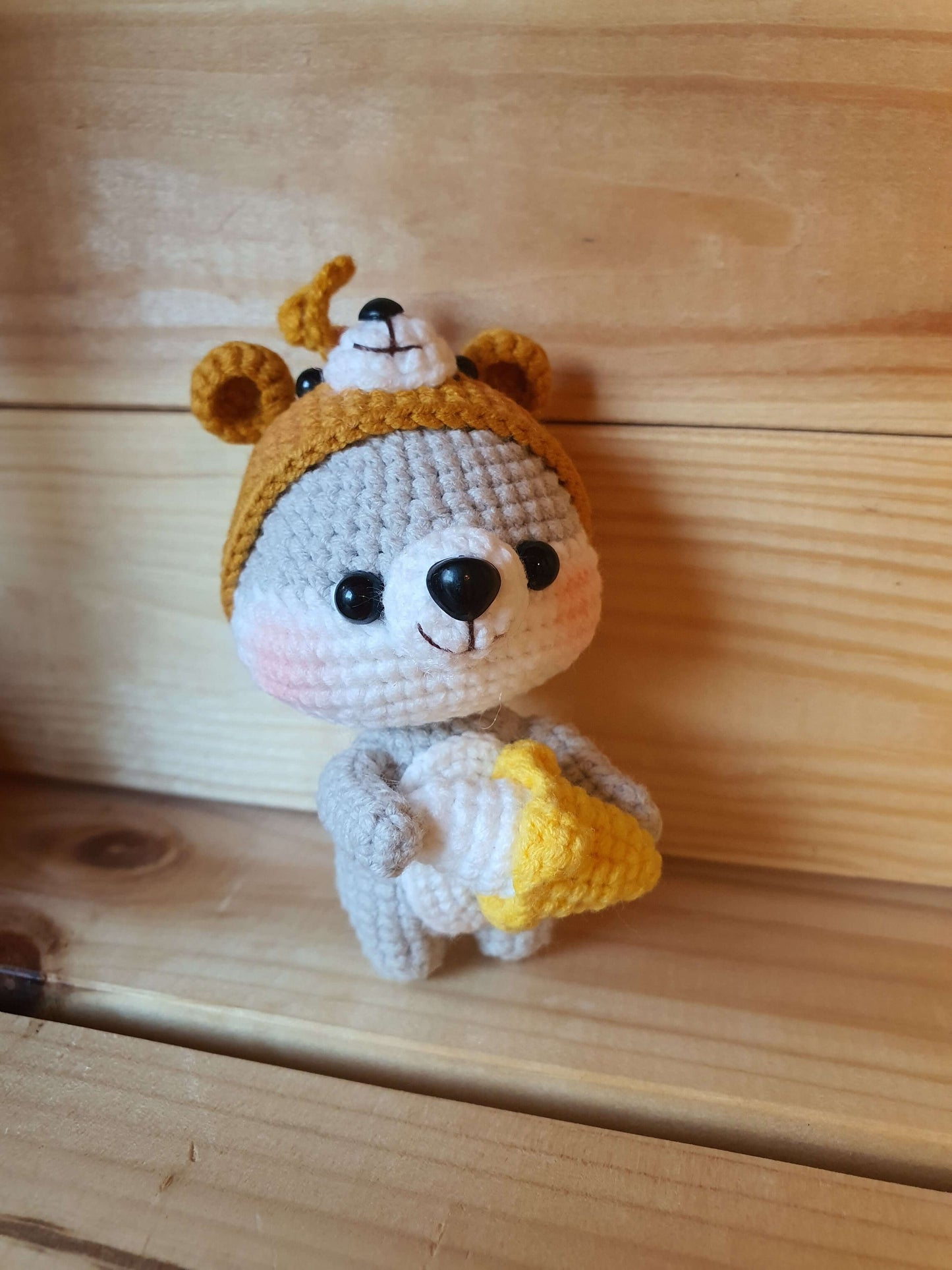 Crocheted bear toy with a yellow hat and honeycomb on a wooden surface