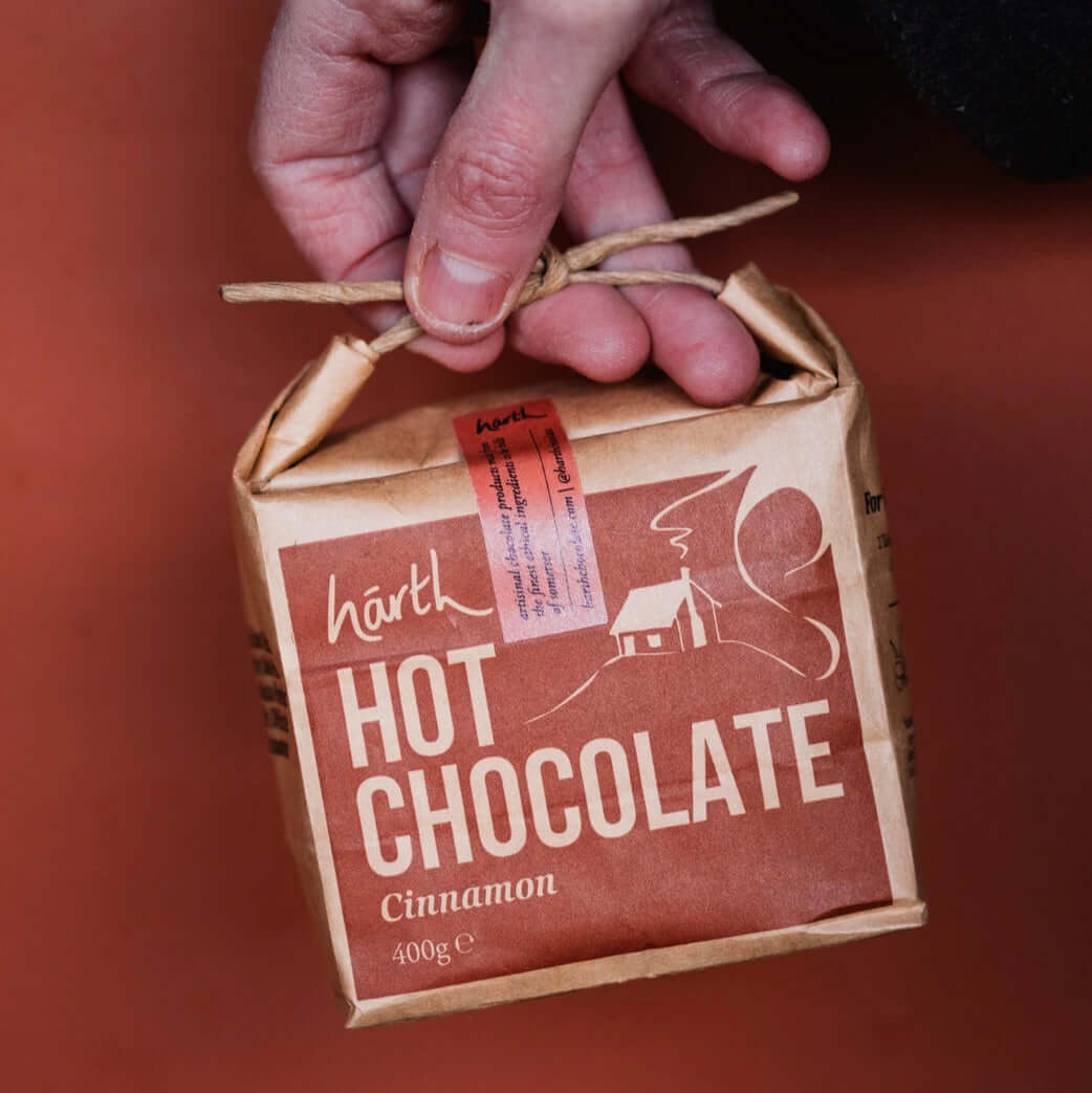 A hand holding a packaged Harth Cinnamon Hot Chocolate mix with a red and brown label.
