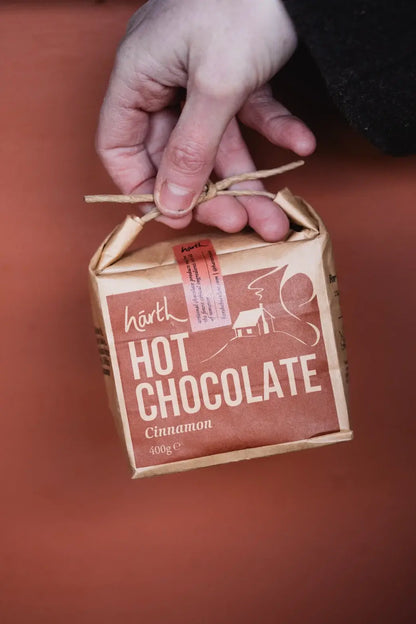 Hand holding a small cardboard box of Hoth Hot Chocolate Cinnamon on a red background