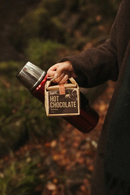 Hand holding a Harth hot chocolate carton and a flask on a woodland walk