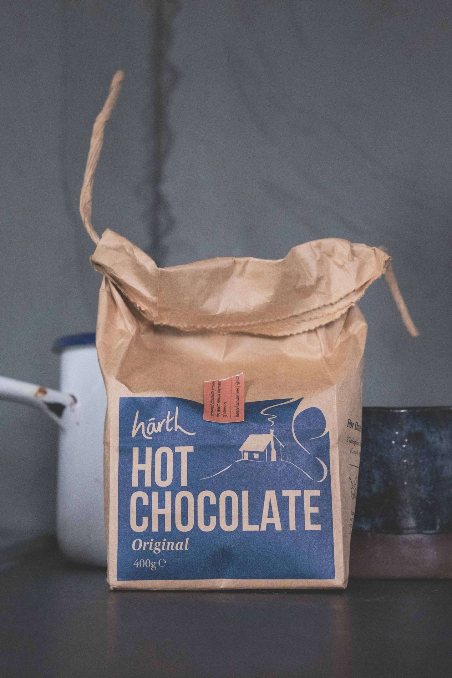 Brown paper bag of Harth Hot Chocolate with a blue label on a dark surface.