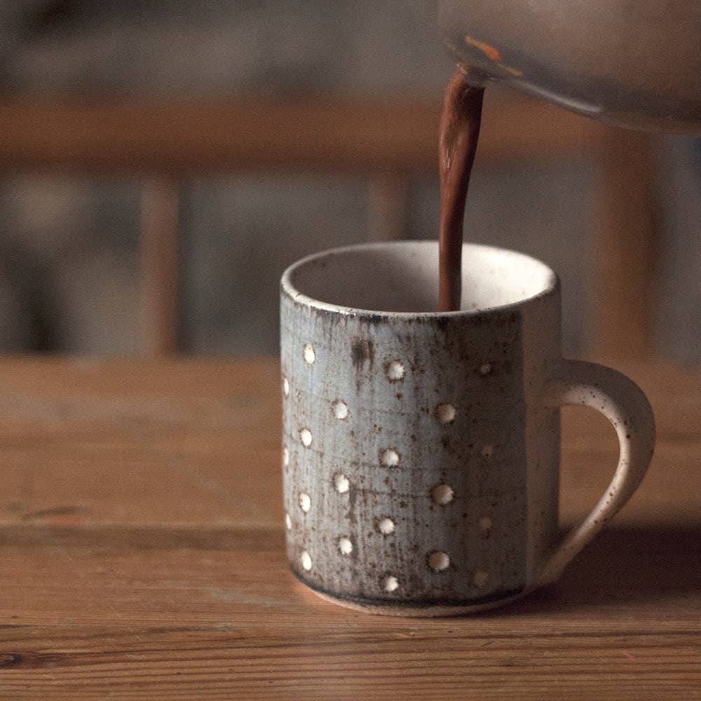 Hot chocolate being poured into a textured mug on a wooden surface