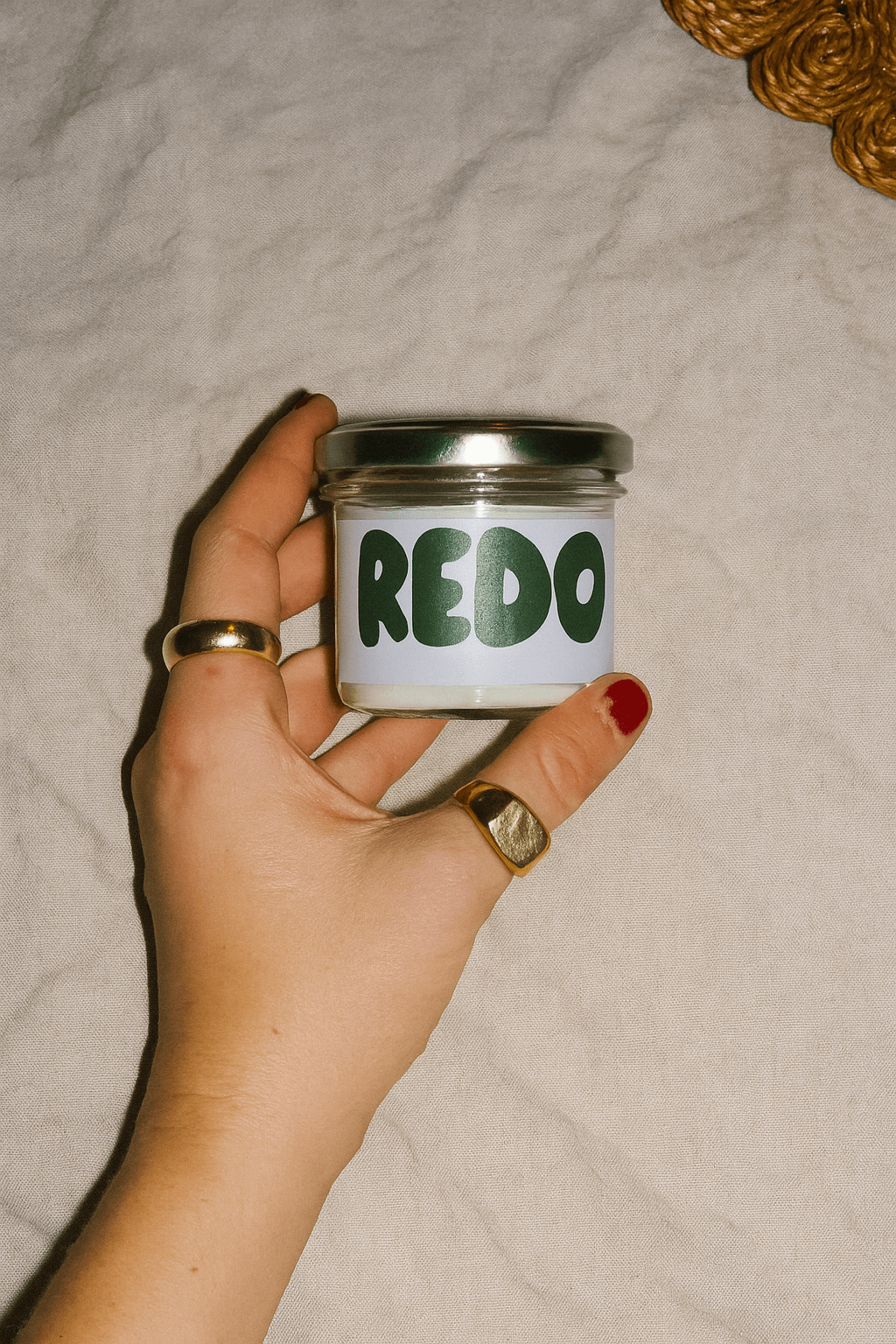 Hand holding a small jar labeled 'REDO' against a neutral background