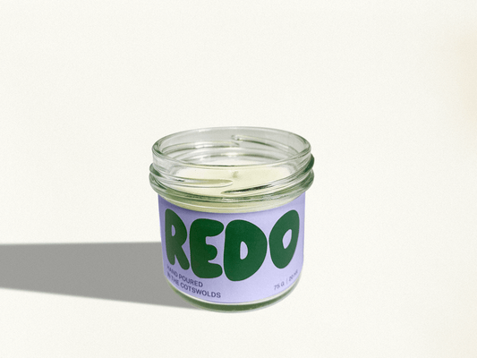 Candle in a glass jar with a purple label and green text on a white background