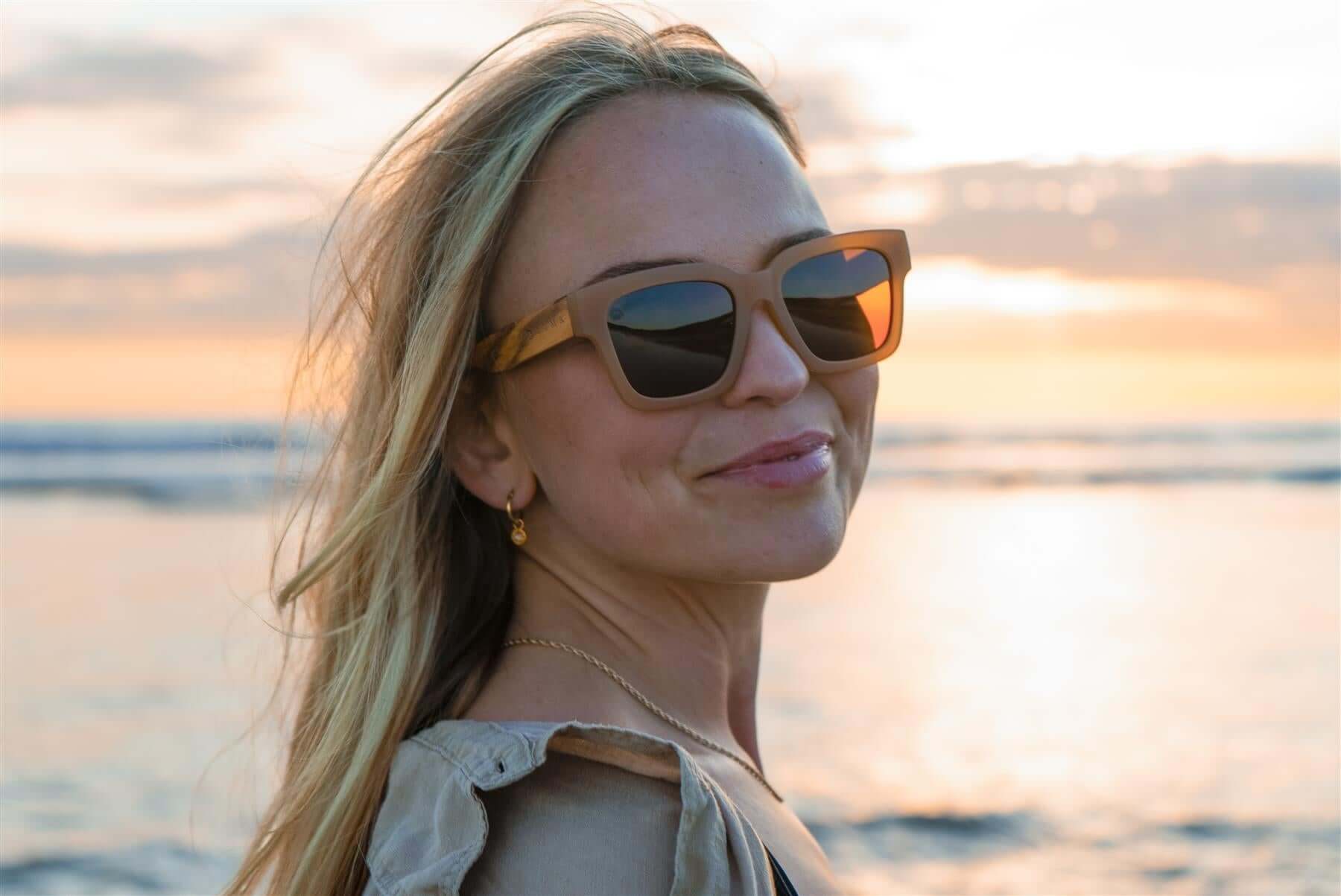 Luma Sunglasses - Polzeath - Brown worn by a woman on a beach during sunset, reflecting an eco-friendly lifestyle.