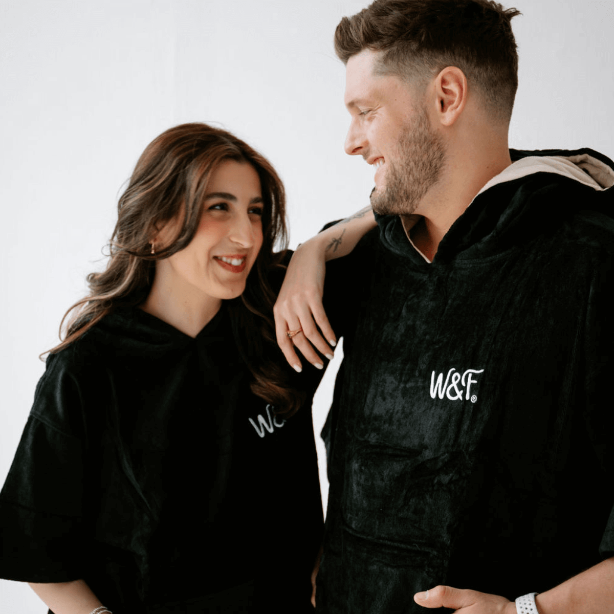 A couple wearing the Luxury Towel Robe, showcasing style and comfort in black organic cotton for beach and poolside lounging.