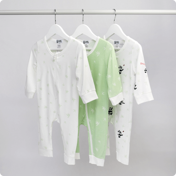 Three baby rompers on hangers against a gray background