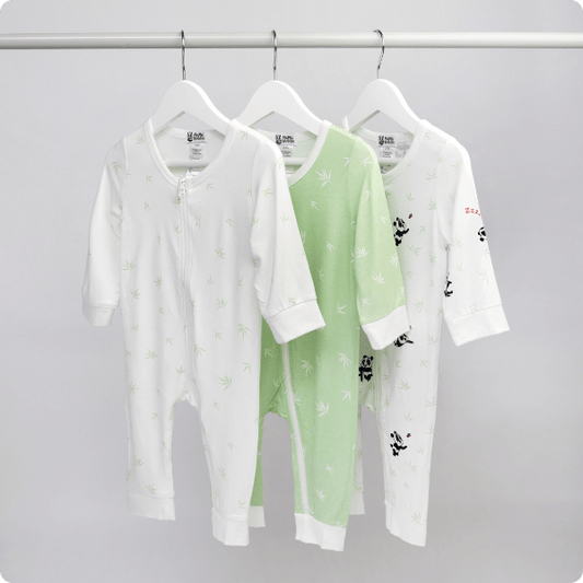 Three baby rompers on hangers against a gray background