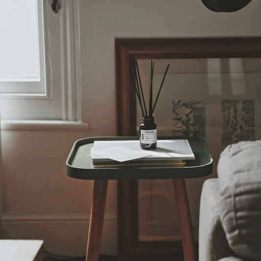 Small round table with a diffuser and papers in a room with a window and wall art.
