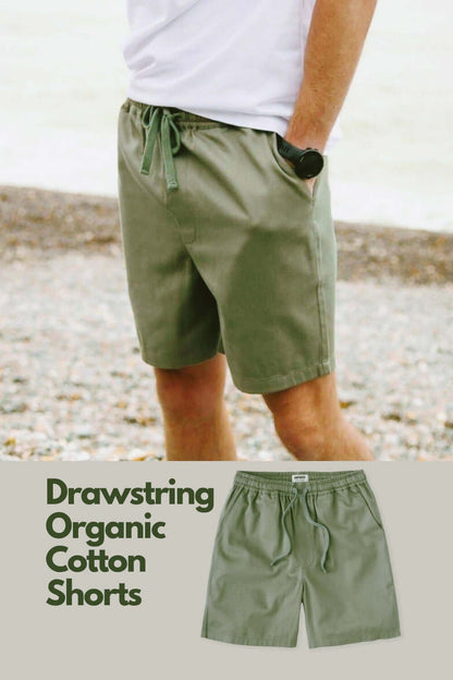 Man wearing Rapanui Sandbar olive green drawstring organic cotton shorts on a pebble beach