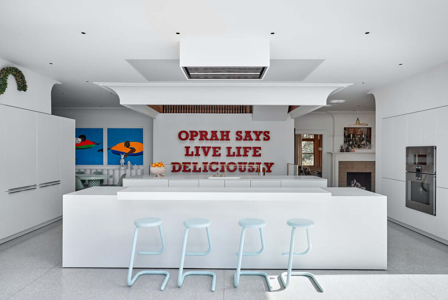 Modern kitchen with a quote on the wall, featuring a white island and stools.