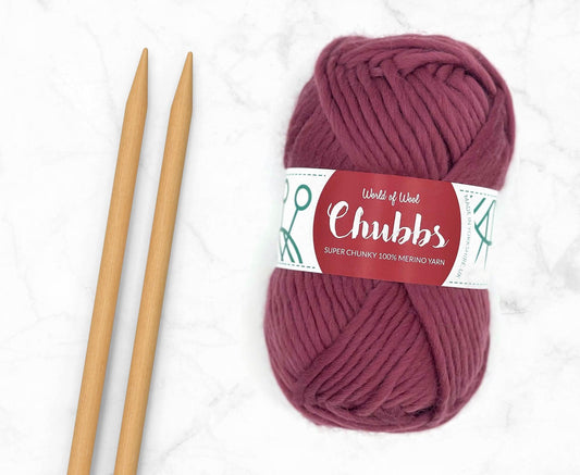Mulberry Merino Super Chunky Weight yarn in fruity red, with knitting needles, showcasing its soft texture.