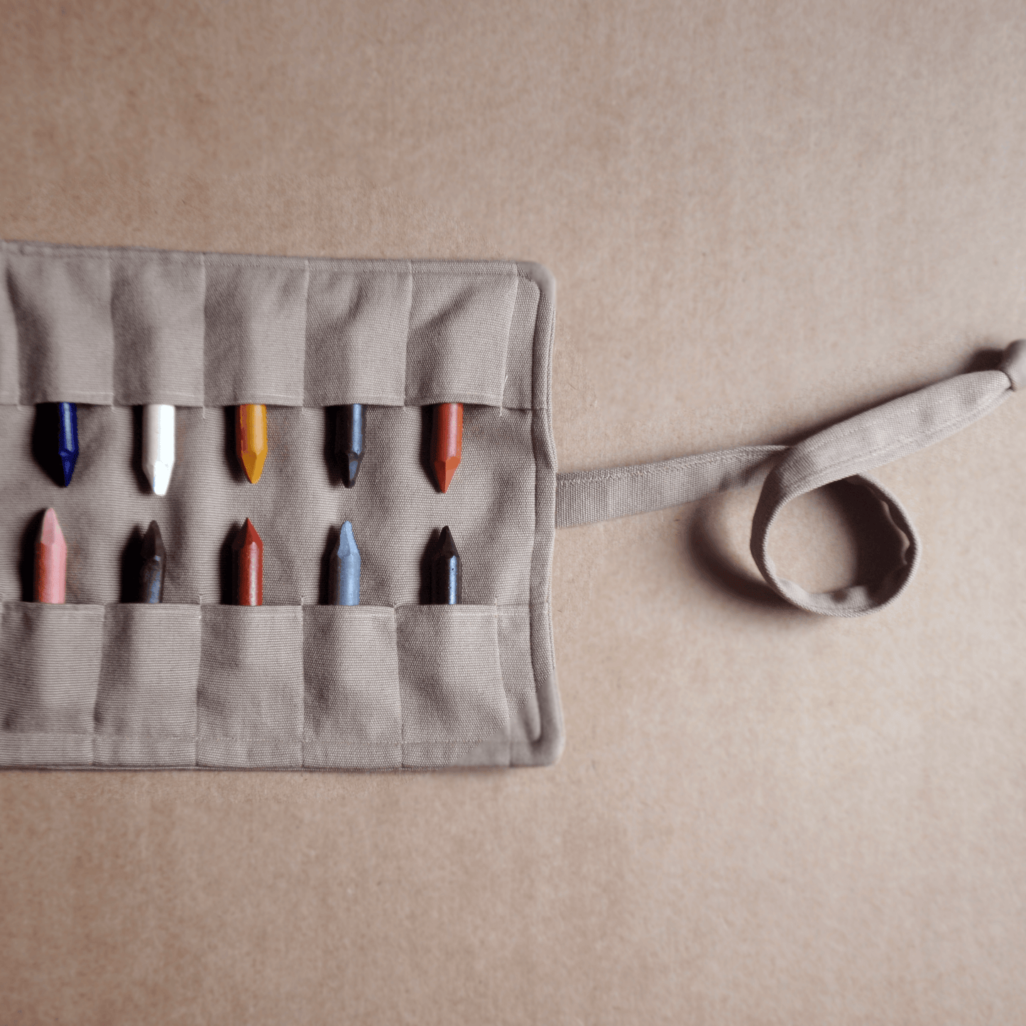 Gray fabric crayon holder with colorful crayons on a beige background