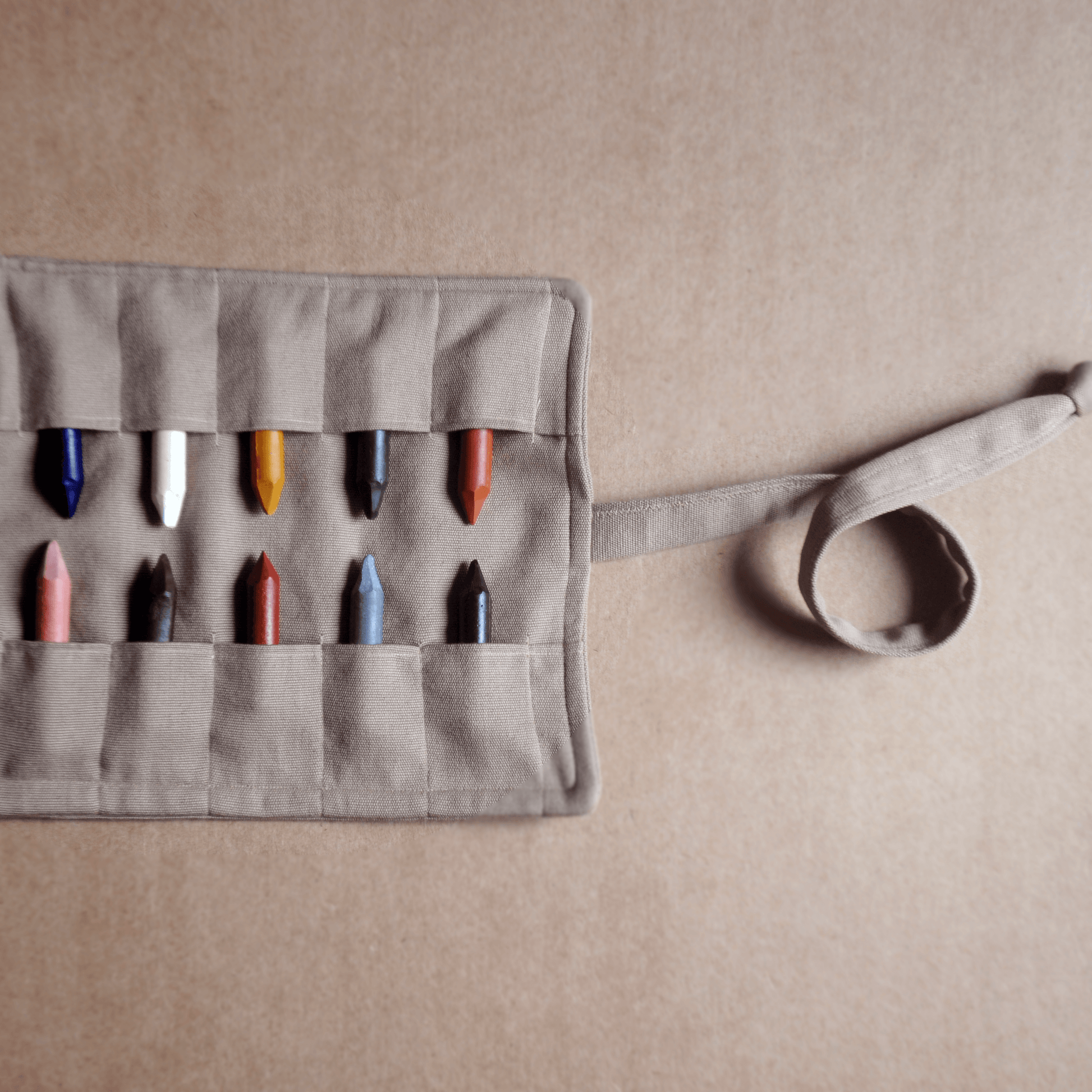 Gray fabric crayon holder with colorful crayons on a beige background