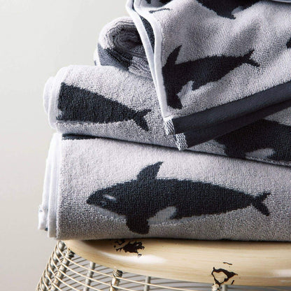 Stack of towels with whale pattern on a wooden stool against a light background
