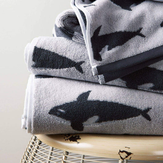 Stack of towels with whale pattern on a wooden stool against a light background