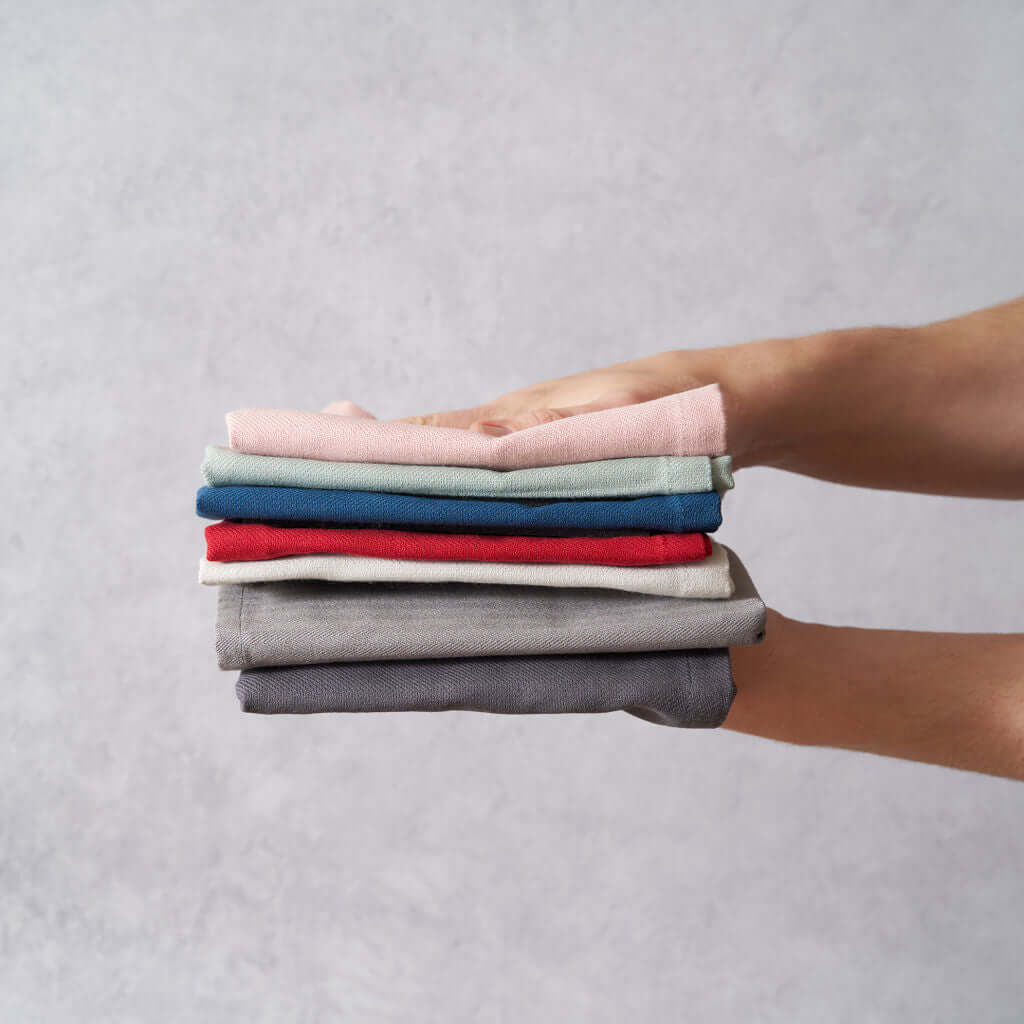 Organic Cotton Tea Towels - Herringbone Weave - Set of 2 stacked in a hand, showcasing vibrant colors and textures.
